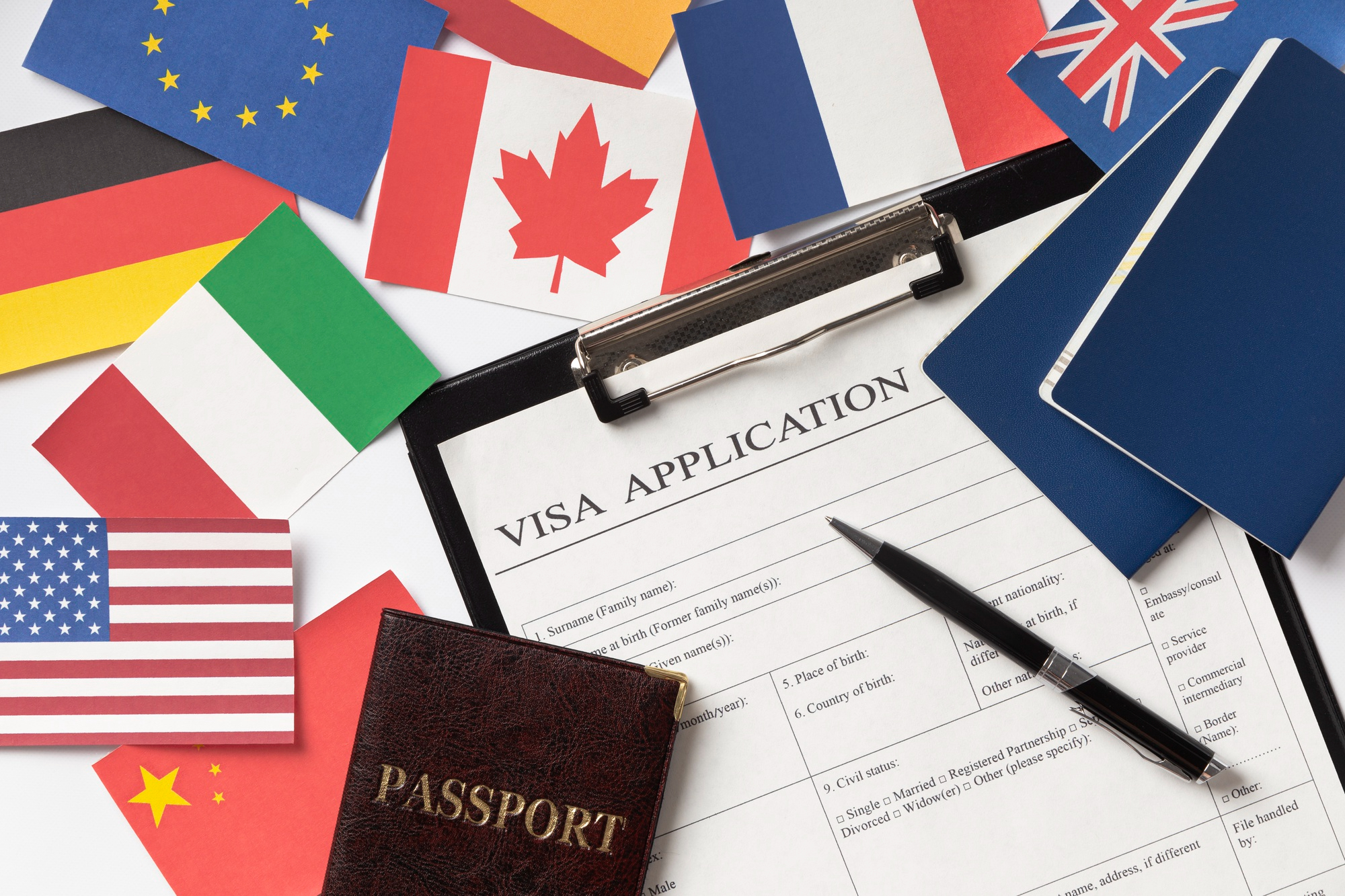 A visa application form, a passport and a pen surrounded by the flags of several countries