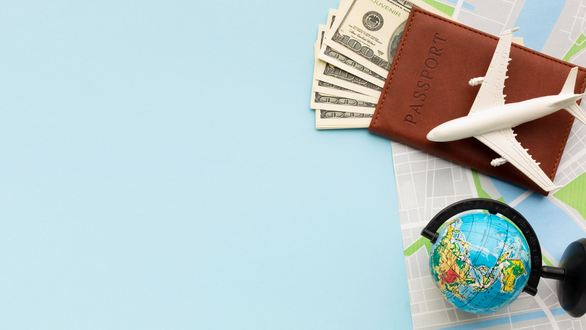 A passport, banknotes, a toy aeroplane and a small globe laid out on a pale blue surface