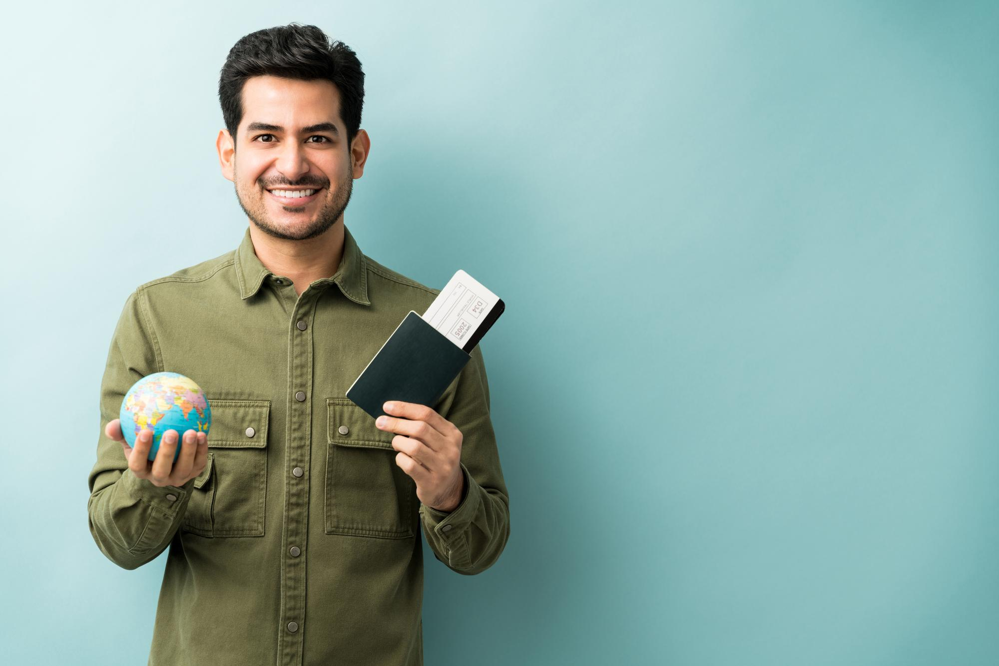 A student holding a globe and a passport against a mint background