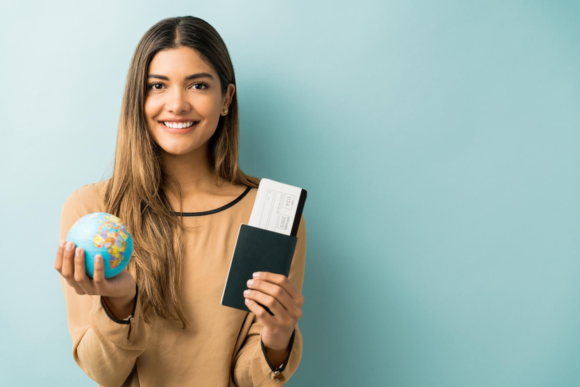 A student holding a small globe and a passport against a mint background